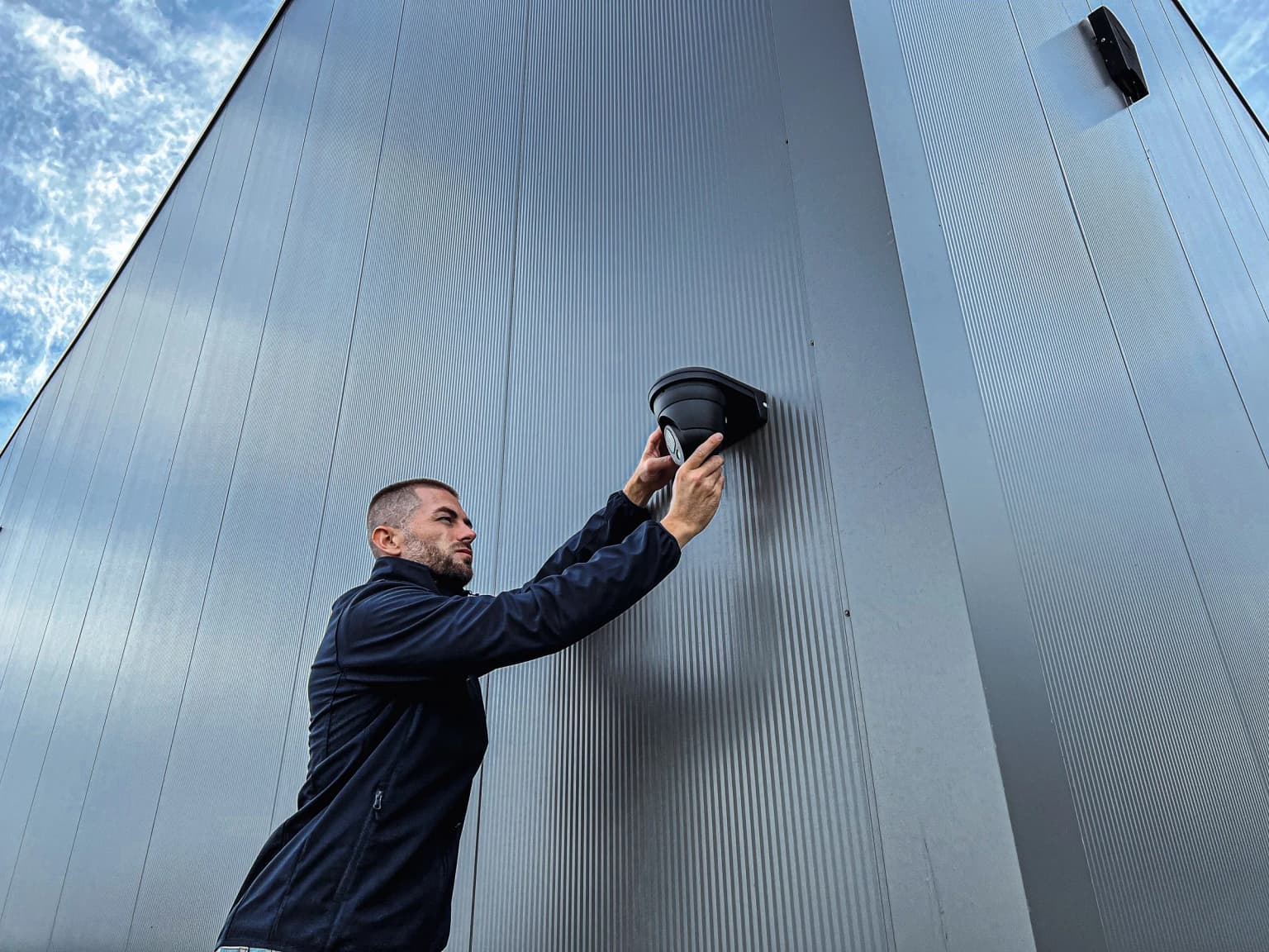 Securetech-monteur installeert een dome-camera op een bedrijfsgevel
