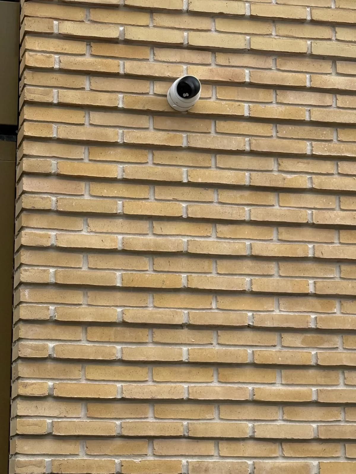 Close-up van compacte dome camera tegen gele bakstenen gevel, VvE Alexliving Rotterdam