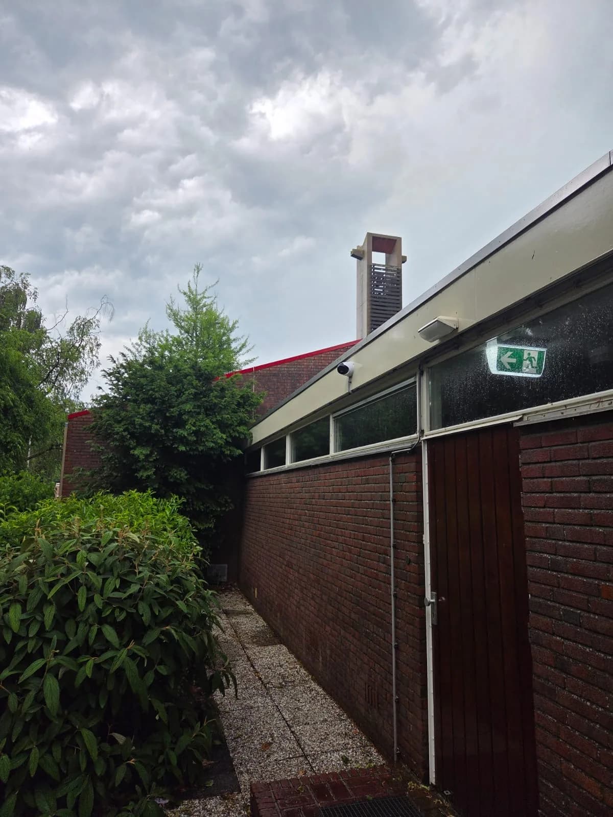 Dome bewakingscamera bij een toegangsdeur en nooduitgang aan de achterzijde van de katholieke kerk in Wognum