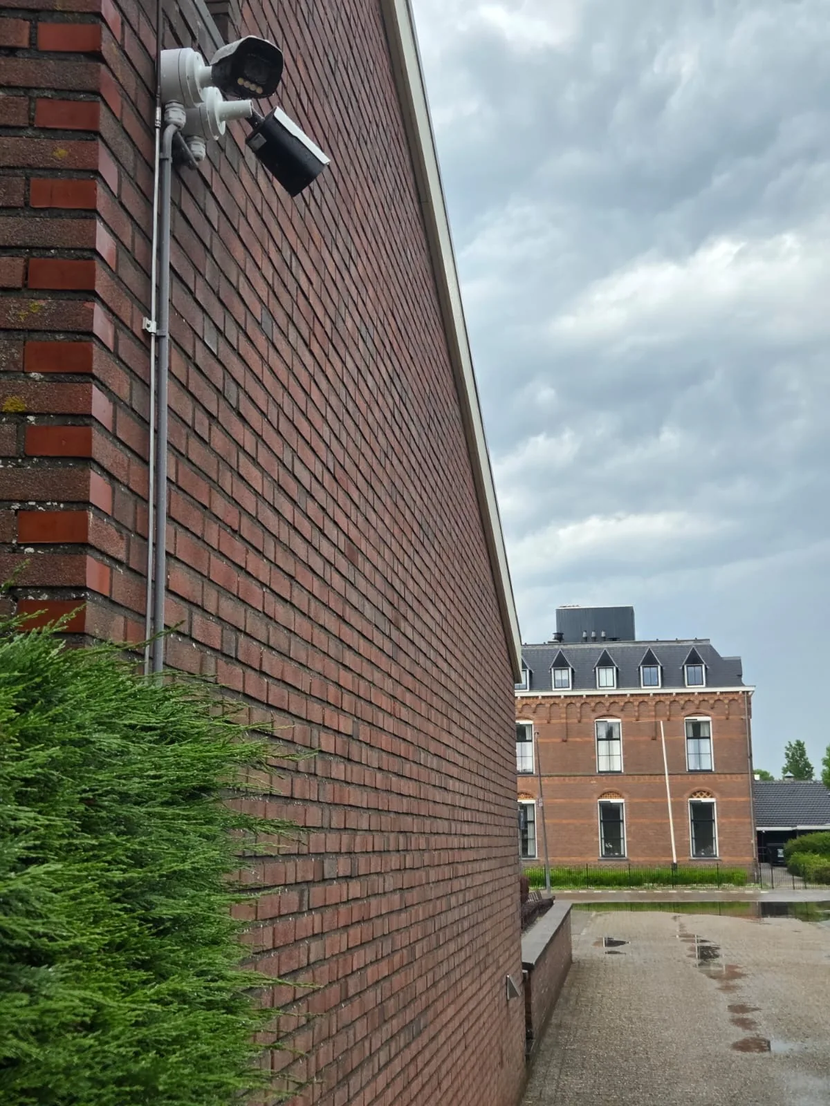 Full-color bullet-camera met zonnekap op de bakstenen gevel, gericht op de oprijlaan naar het parkeerterrein van de kerk in Wognum