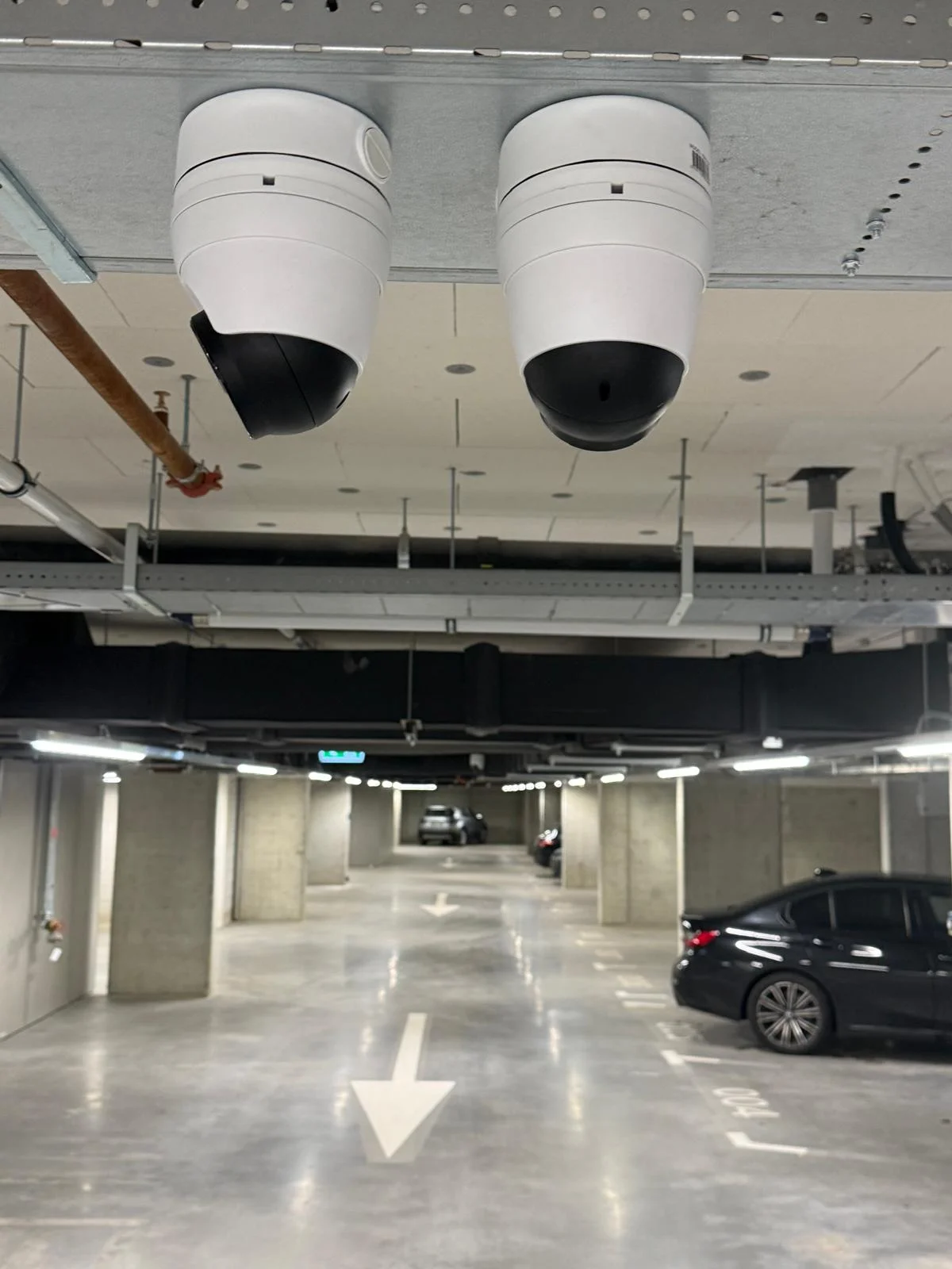 Twee PTZ domes naast elkaar aan plafond parkeergarage met doorkijk op rij parkeerplekken