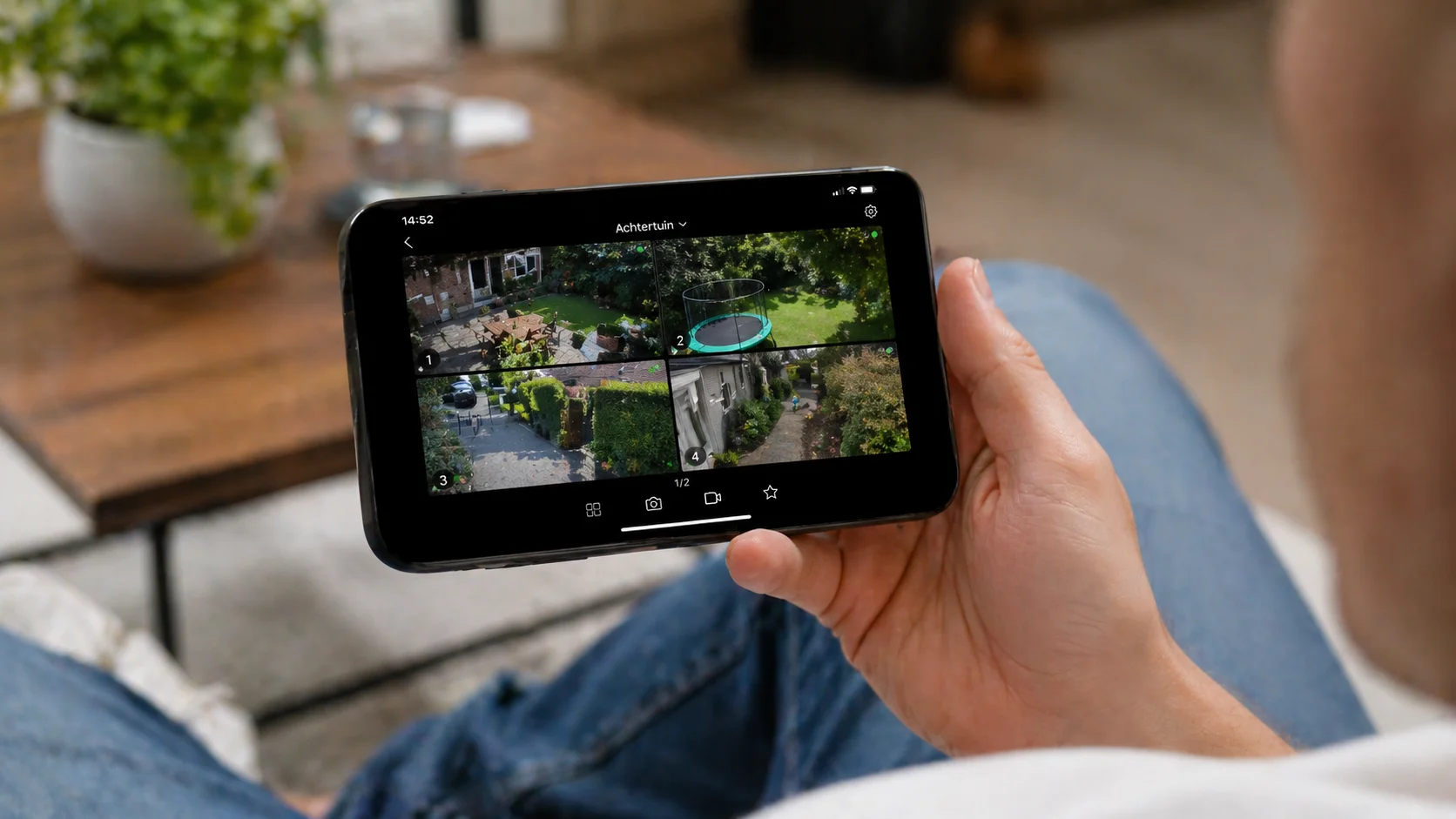 Hand met een smartphone die een live multi-channel camera-grid van een woning toont via de app
