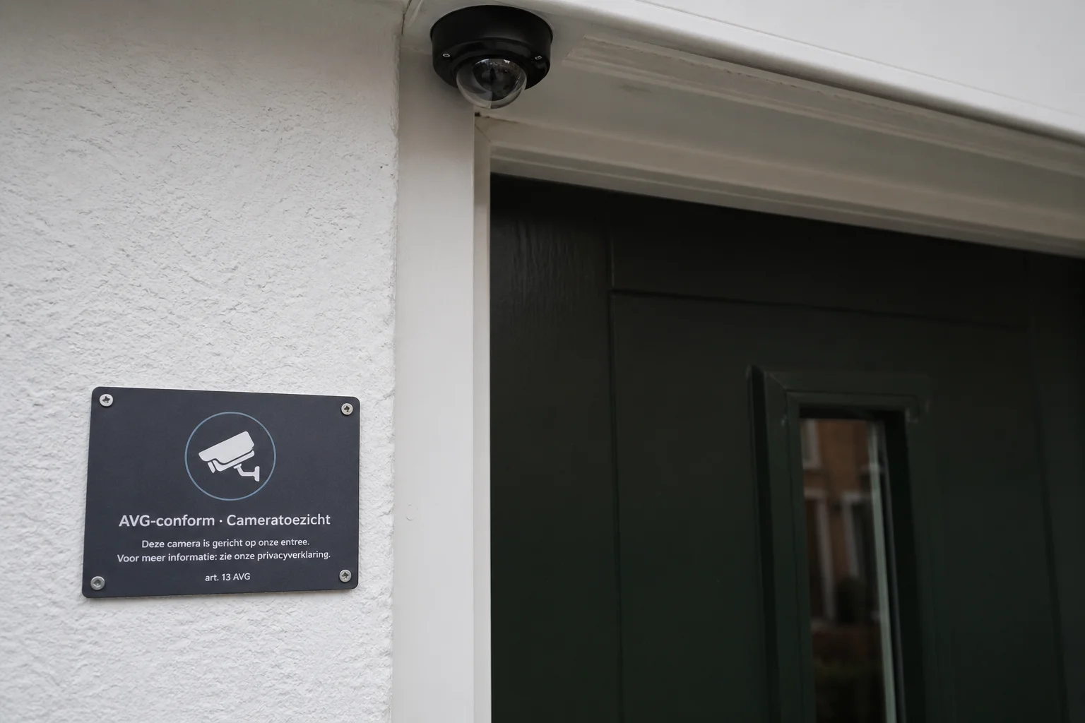 Close-up van een AVG-conform Cameratoezicht-plaatje naast een Nederlandse voordeur met camera subtiel zichtbaar
