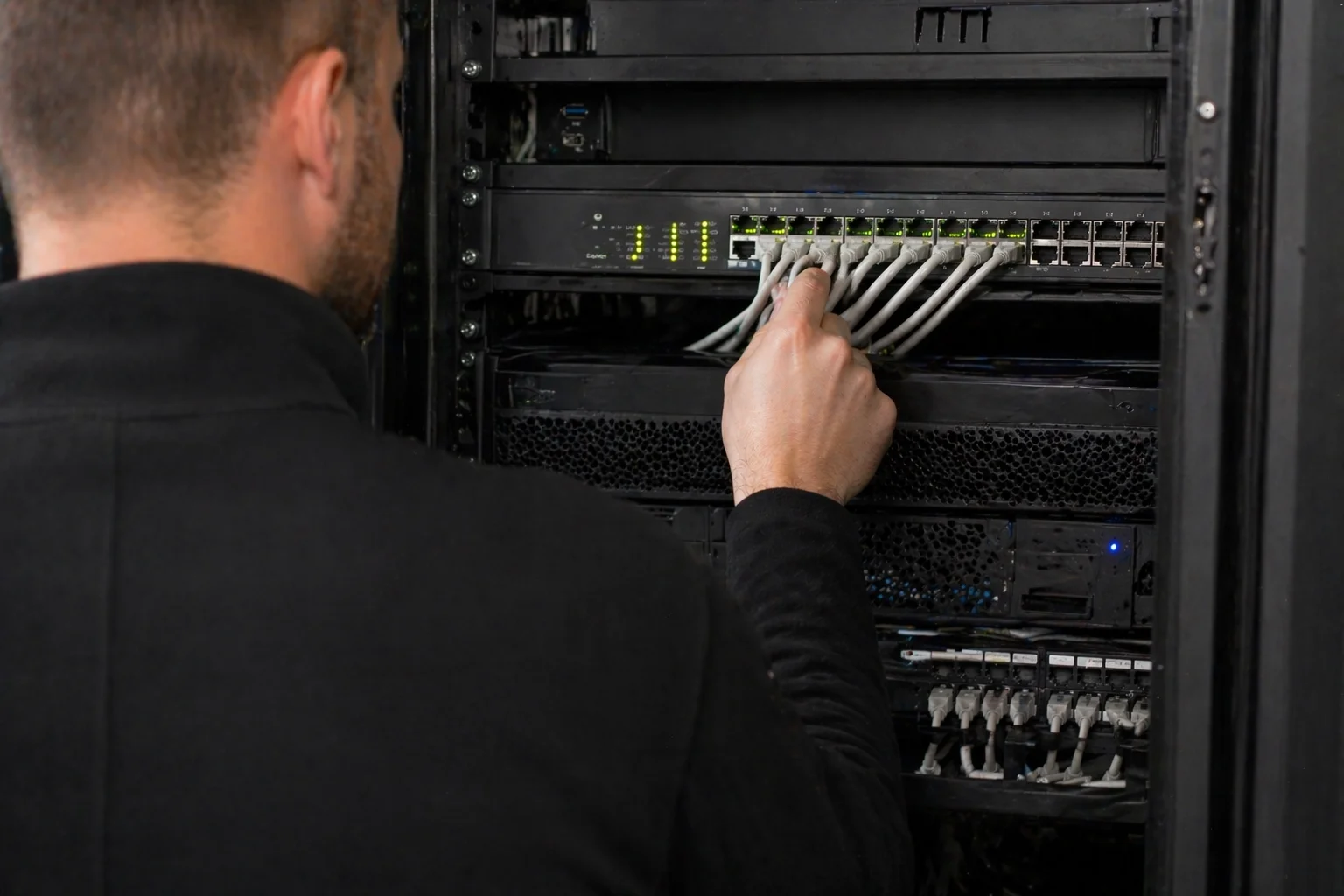 Securetech-monteur sluit meerdere ethernetkabels aan op een PoE-switch in een serverkast met brandende LEDs