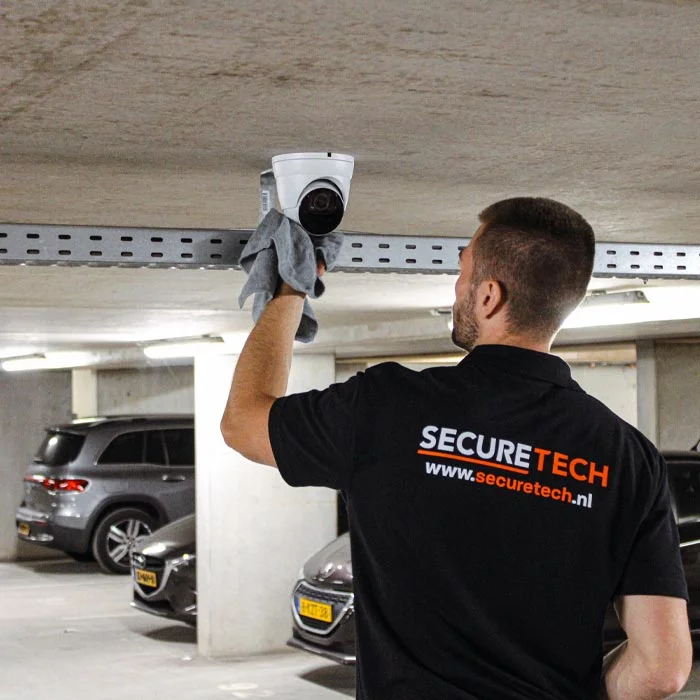 Securetech-monteur reinigt een dome-camera in een parkeergarage met een microvezeldoek