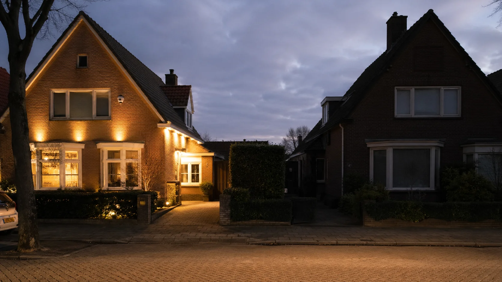 Nederlandse straat bij dusk: een verlichte woning met zichtbare beveiligingscamera contrasterend met een donkere woning ernaast