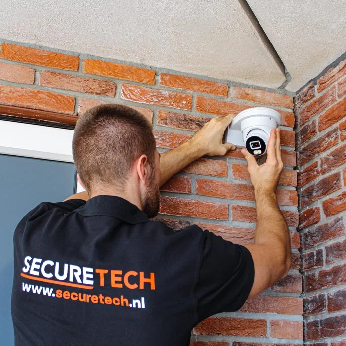 Securetech-monteur installeert een witte dome-camera bij een Nederlandse voordeur onder bakstenen overkapping