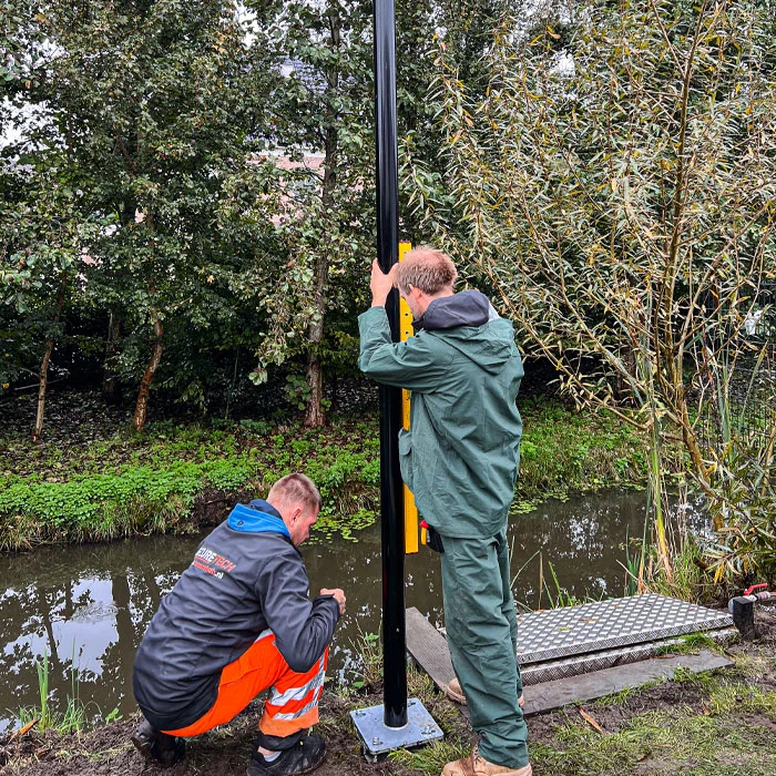 Twee Securetech-monteurs samen aan het werk bij het plaatsen van een cameramast op een buitenterrein