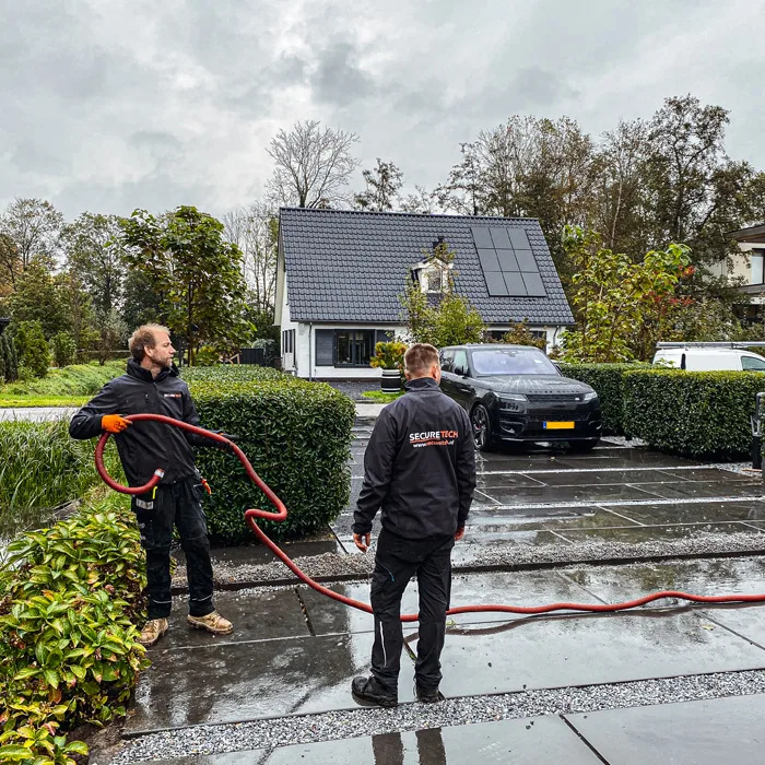 Twee Securetech-monteurs trekken netwerkkabels op de oprit van een Nederlandse woning in de regen