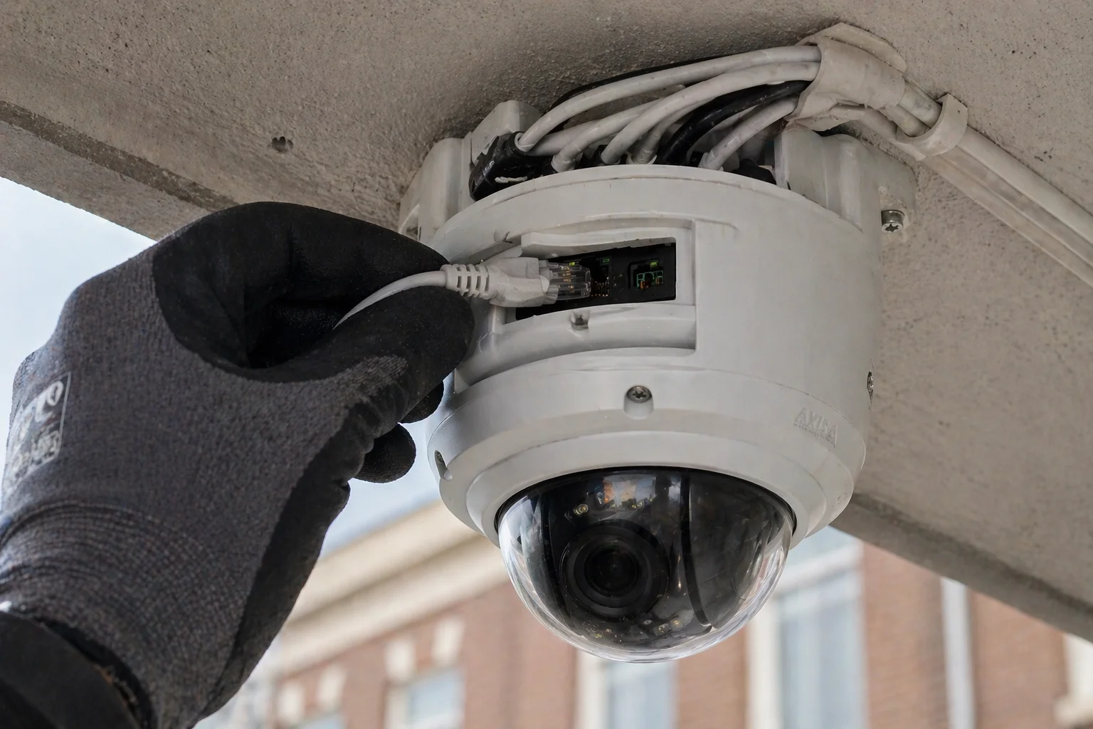 Hand steekt een RJ45-ethernetstekker in de achterkant van een witte IP-dome-camera